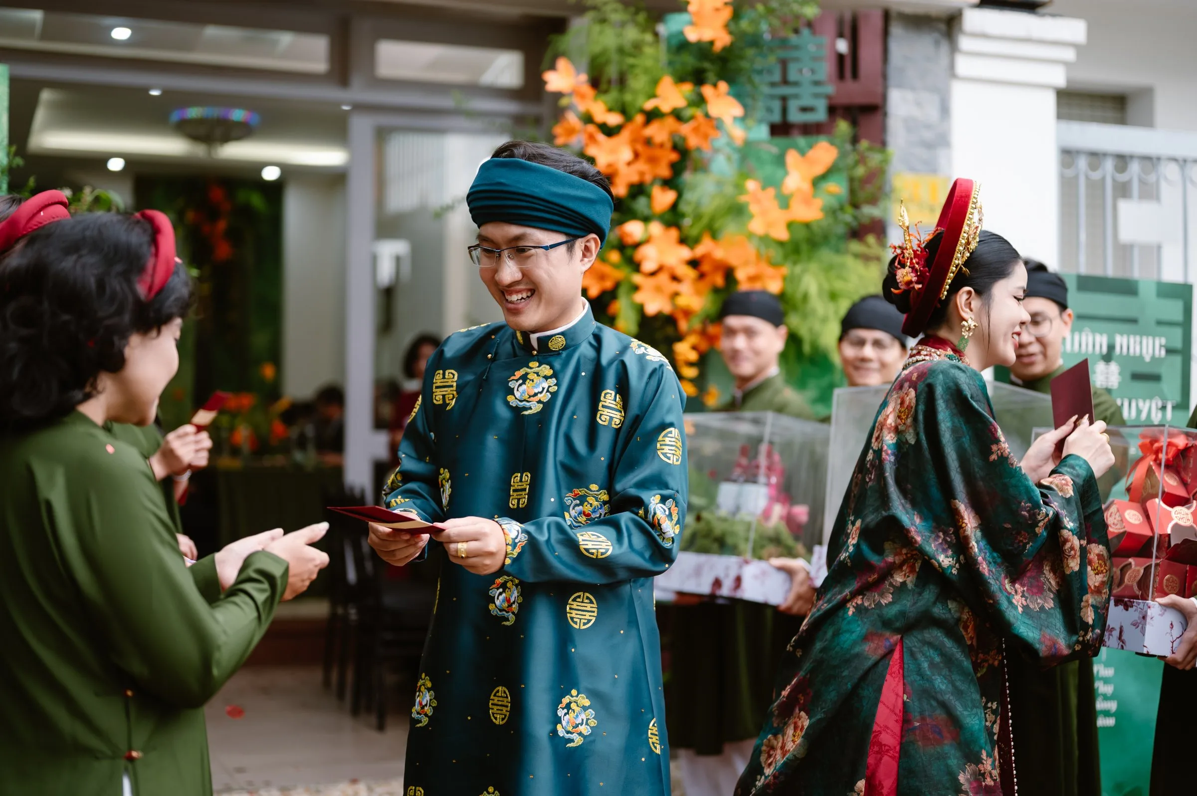 A groom in a blue ao dai presenting a red envelope to a family elder during a traditional Vietnamese wedding.