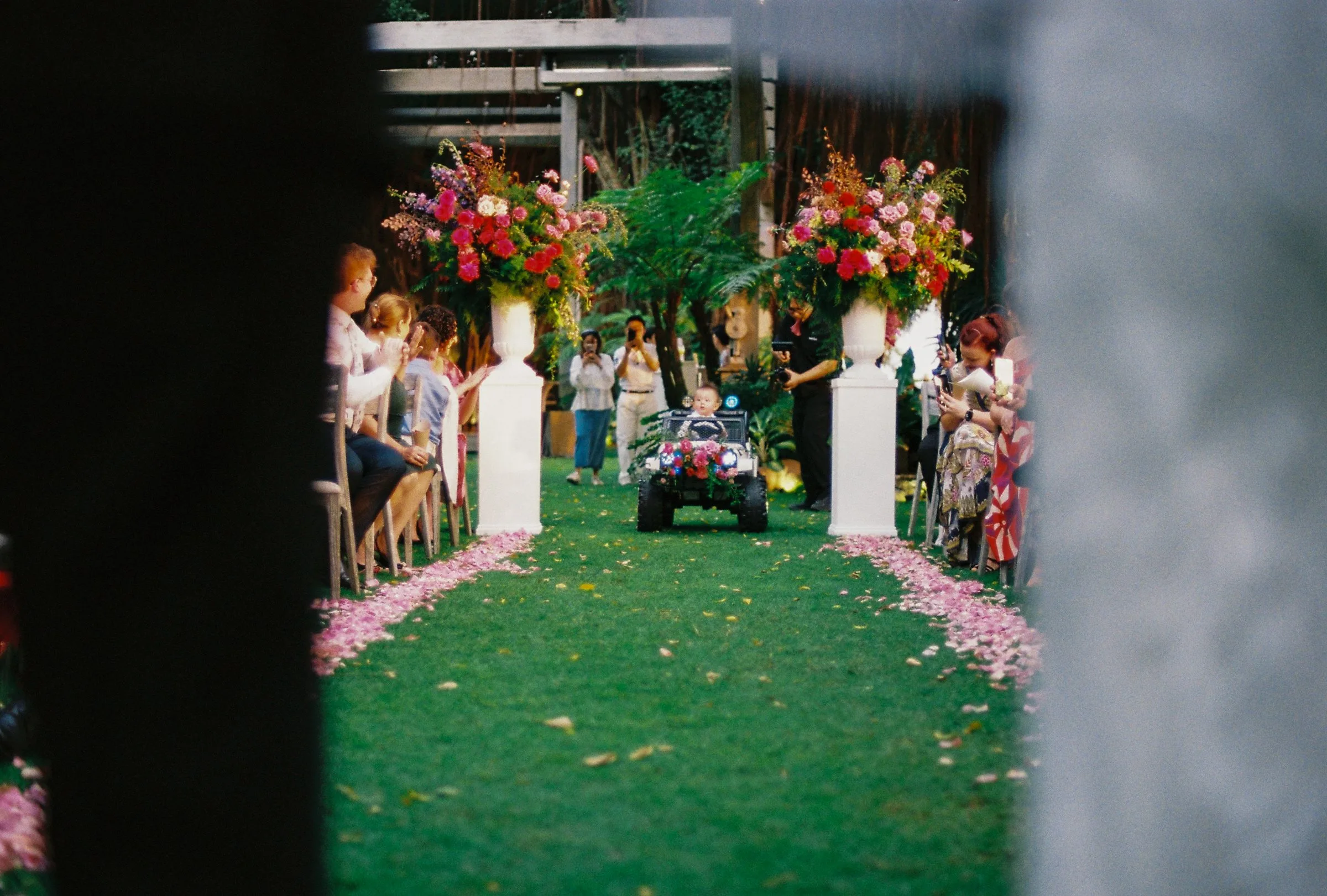 A ring bearer driving a toy car down the petal aisle, film wedding