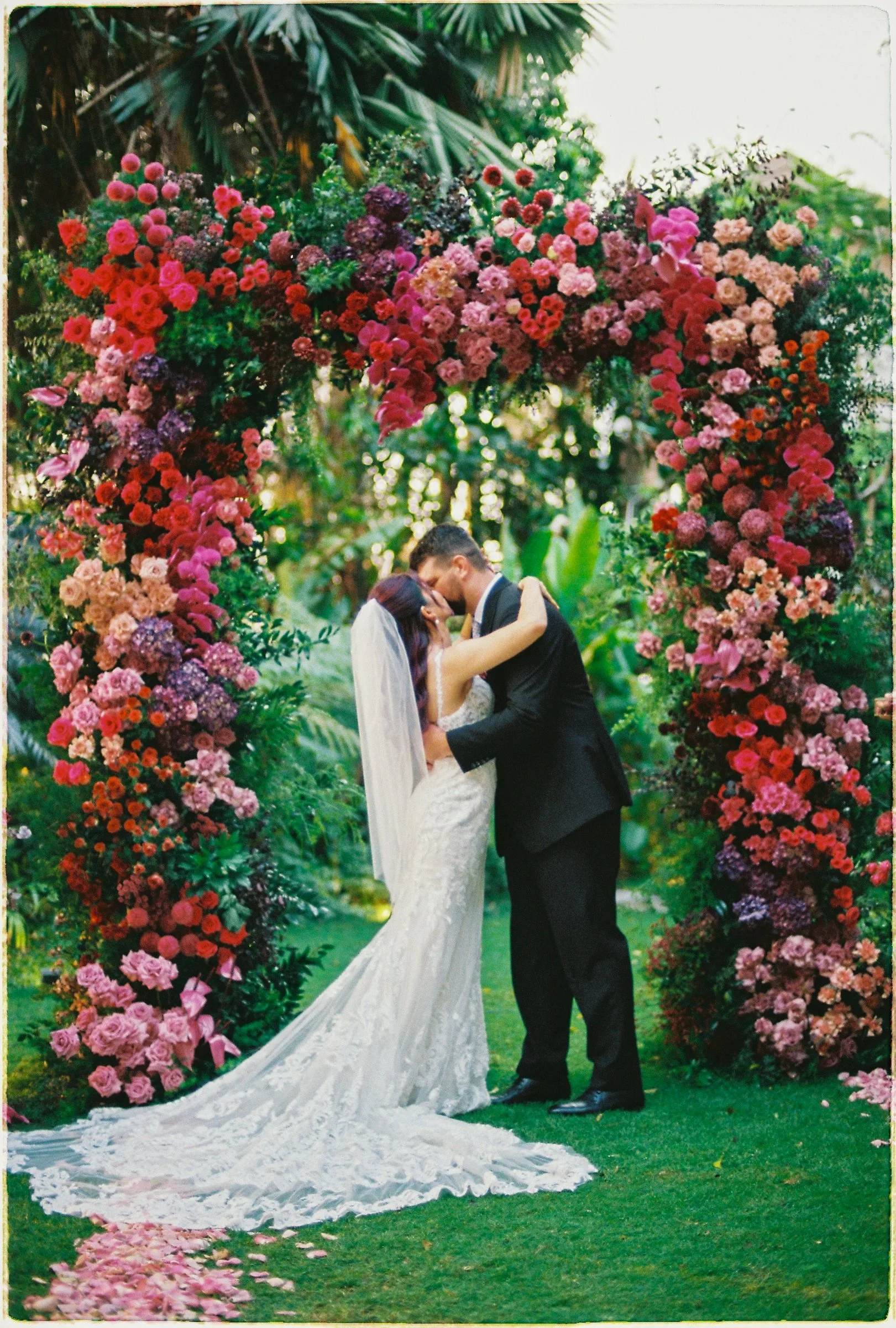 Bride and groom's first kiss under a lush floral arch at a film wedding at An Lam Retreats by TIMO Wedding