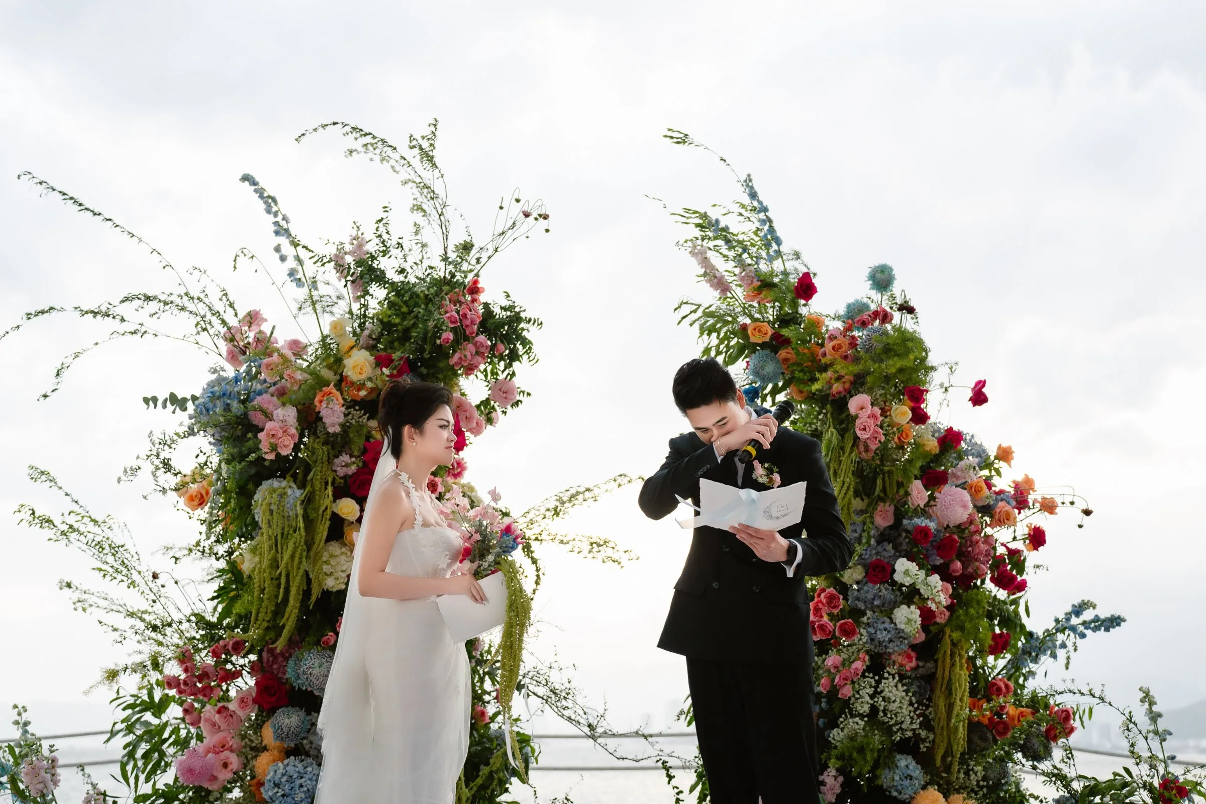 Bride and groom reading their vows at a floral arch by the sea in Nha Trang