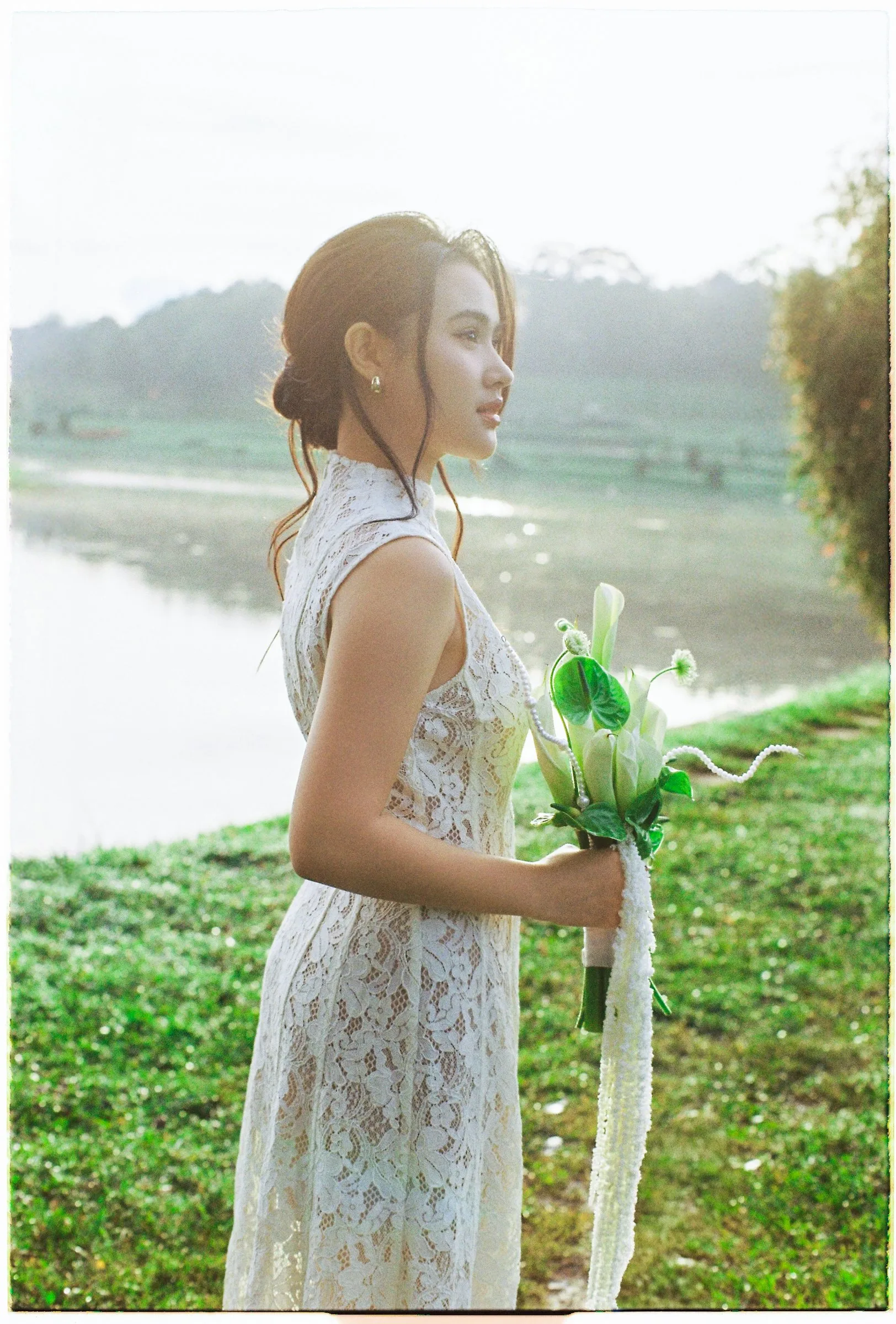 Bride in a lace dress by a Da Lat lake at golden hour, film pre-wedding