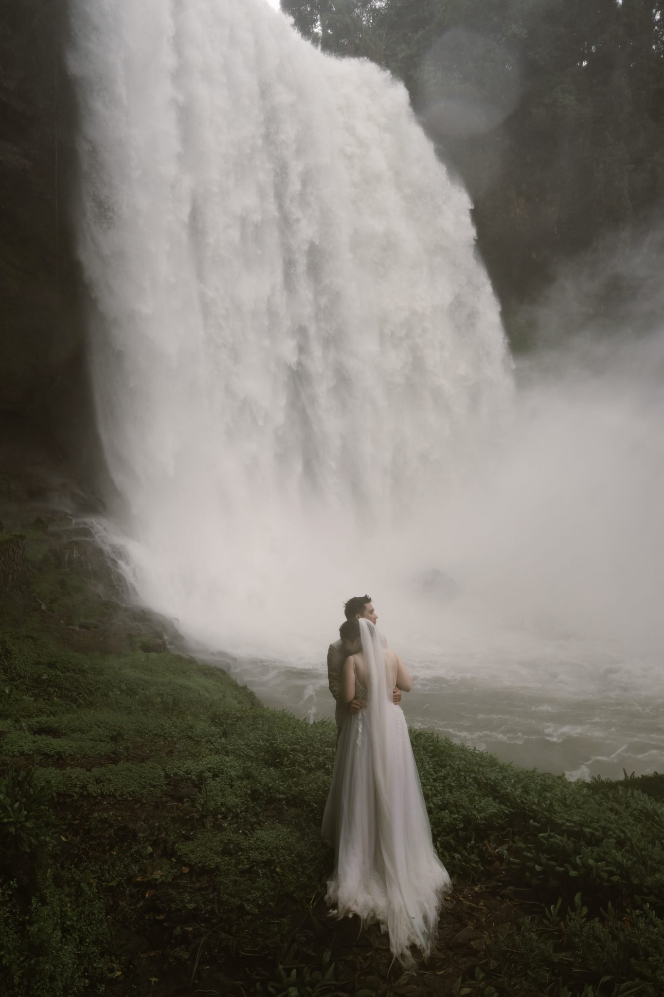 My in front of the falls, her veil and gown catching the spray.