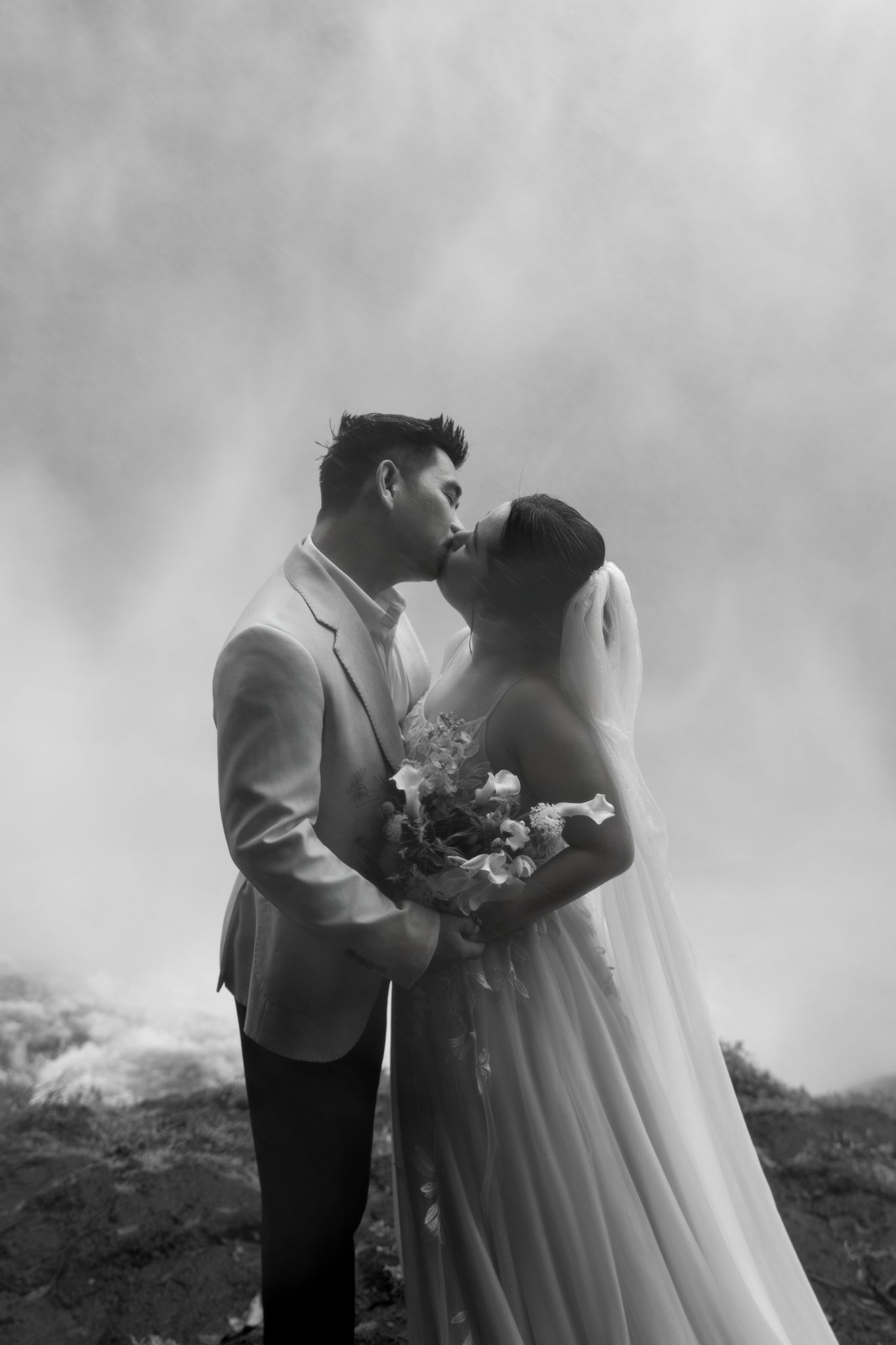 A kiss in the mist, bouquet in hand, the rain doing its own thing around them.