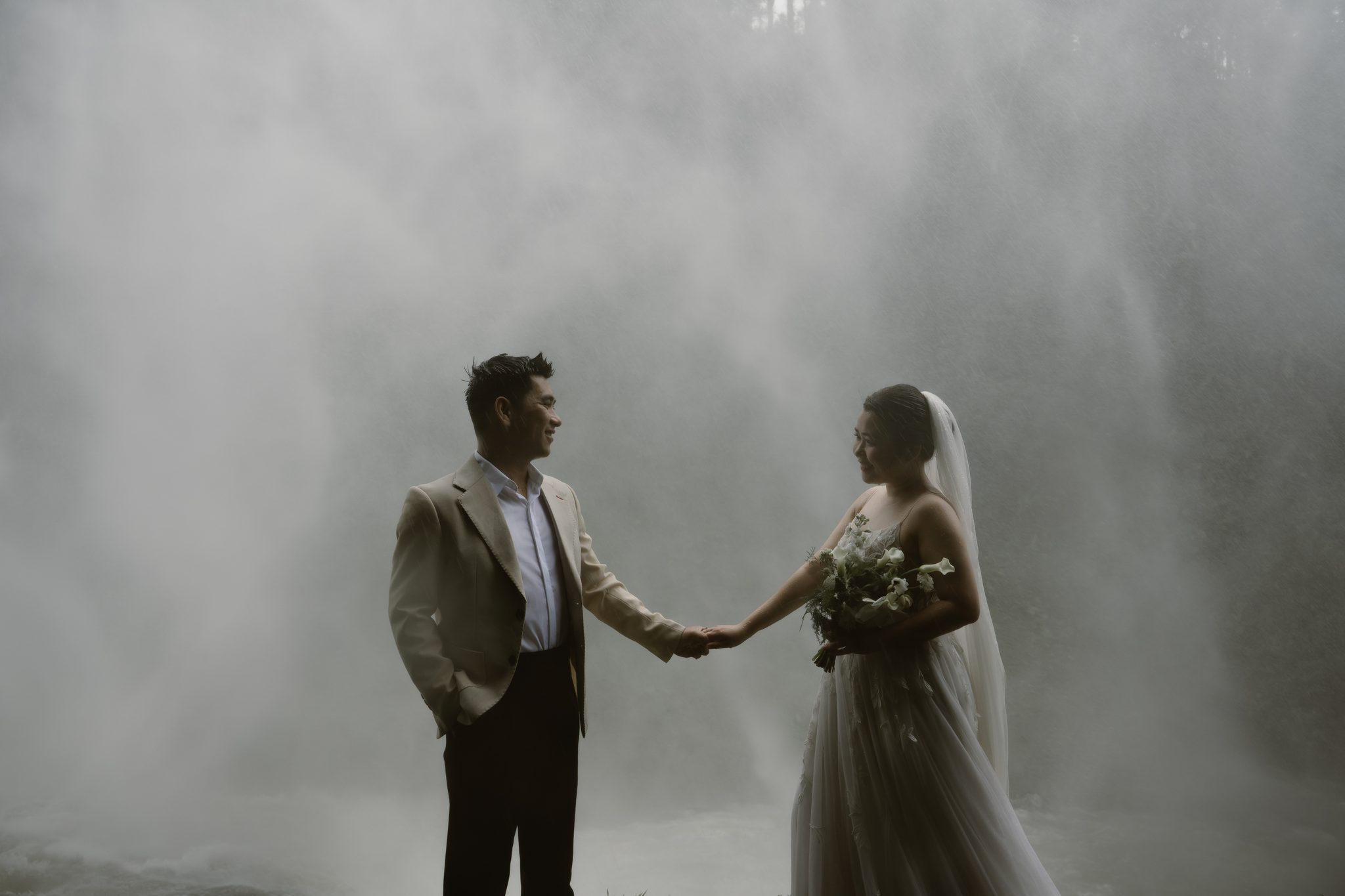 Hand in hand in the thick of the spray, the falls a wall of white behind them.