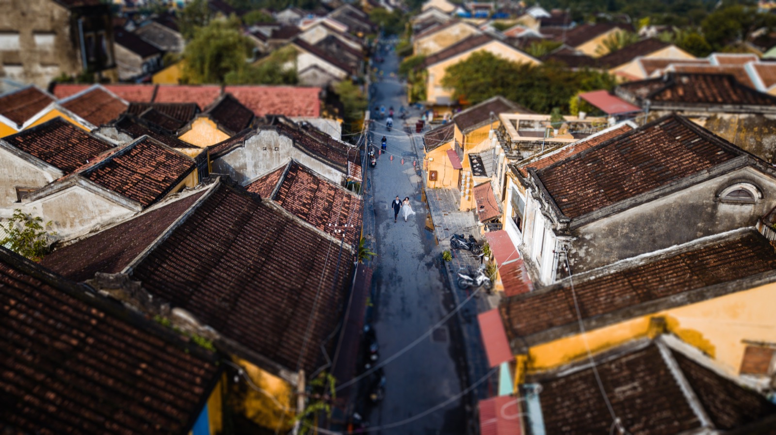 From above, two small figures on a quiet old-town street among the tiled roofs.