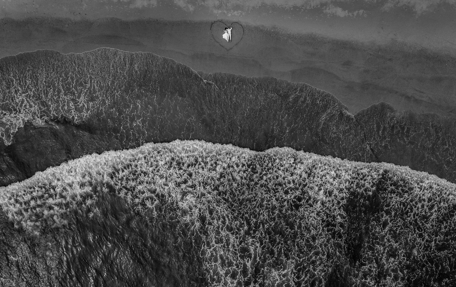 A heart drawn in the sand, and the couple inside it, seen from the air.