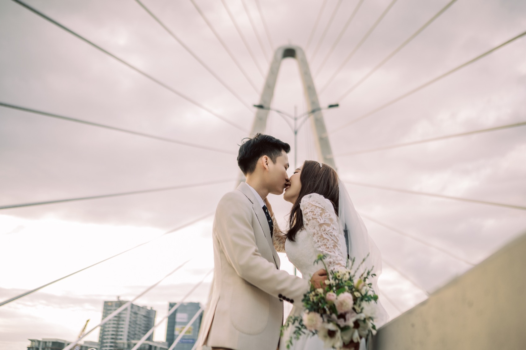 Couple kissing on a bridge with the Ho Chi Minh City skyline behind them
