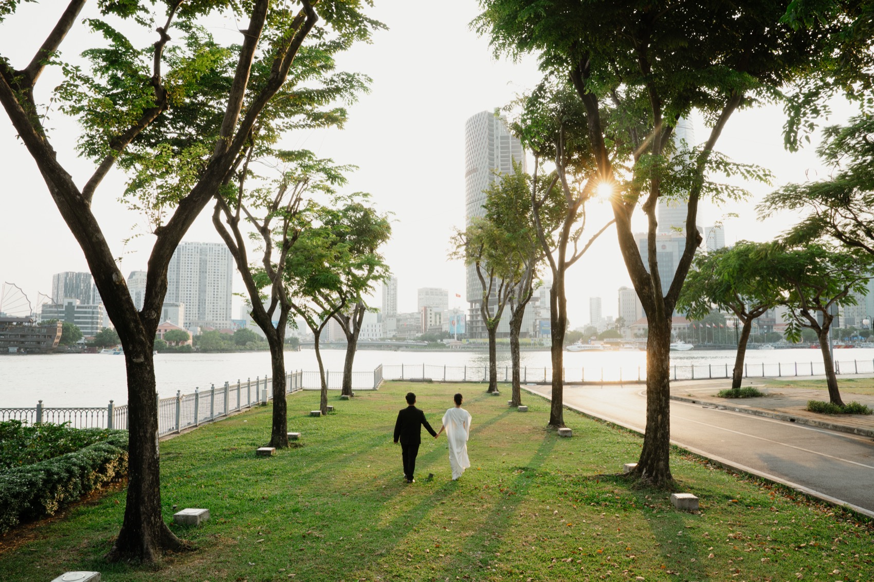 Couple in a riverside park at golden hour with the Saigon skyline across the water