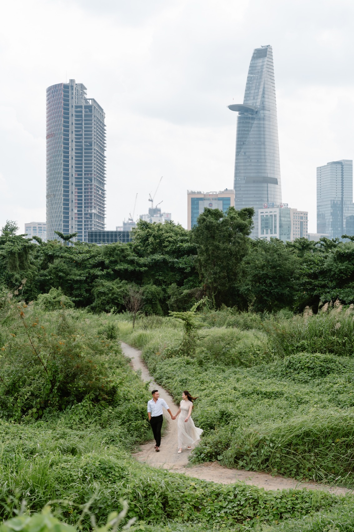 Couple walking a grassy path with the District 1 skyline behind, Ho Chi Minh City