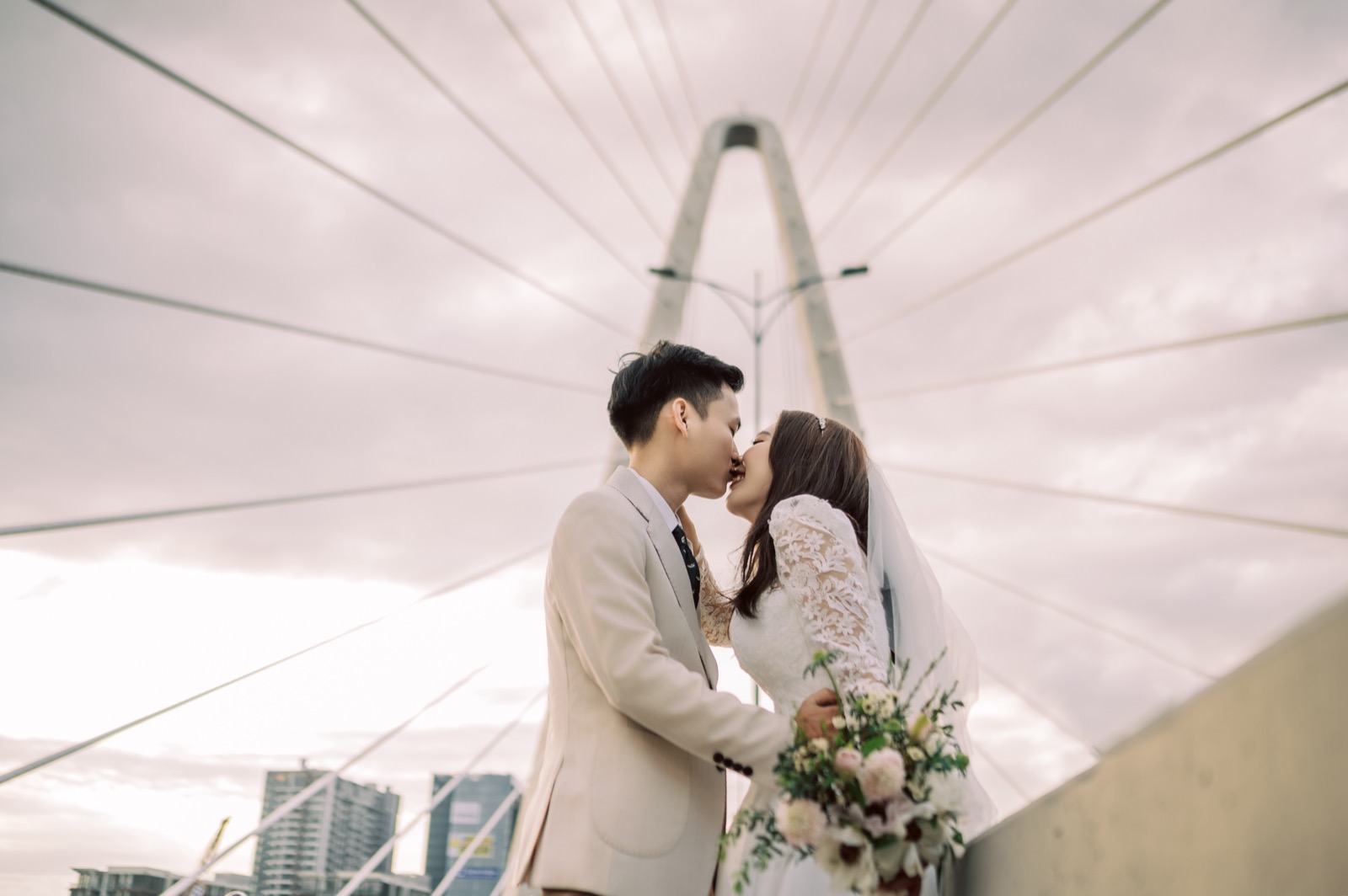A kiss on the bridge as the Ho Chi Minh City skyline glows behind them.