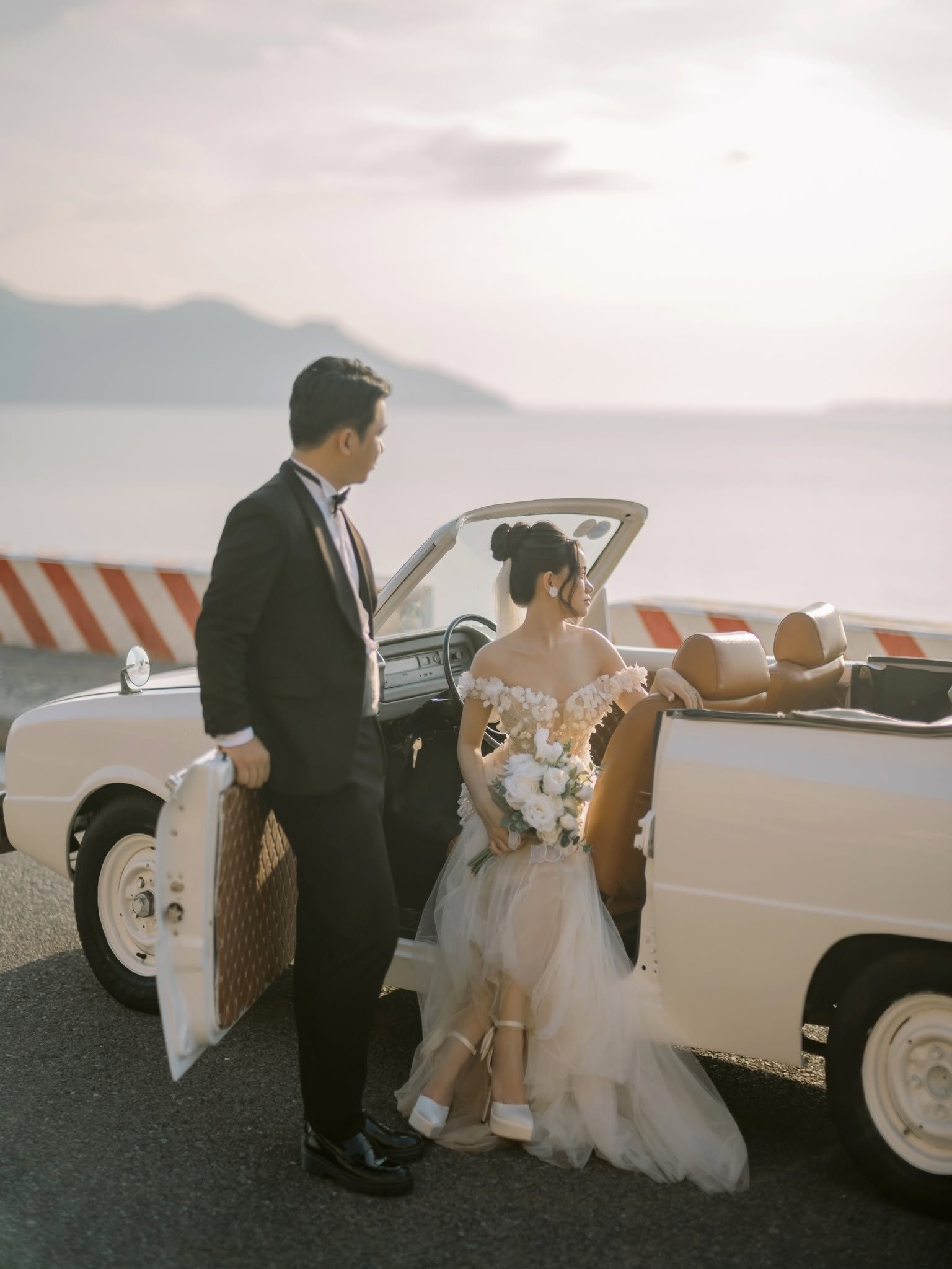 By the open door of the classic car, the sea behind them.
