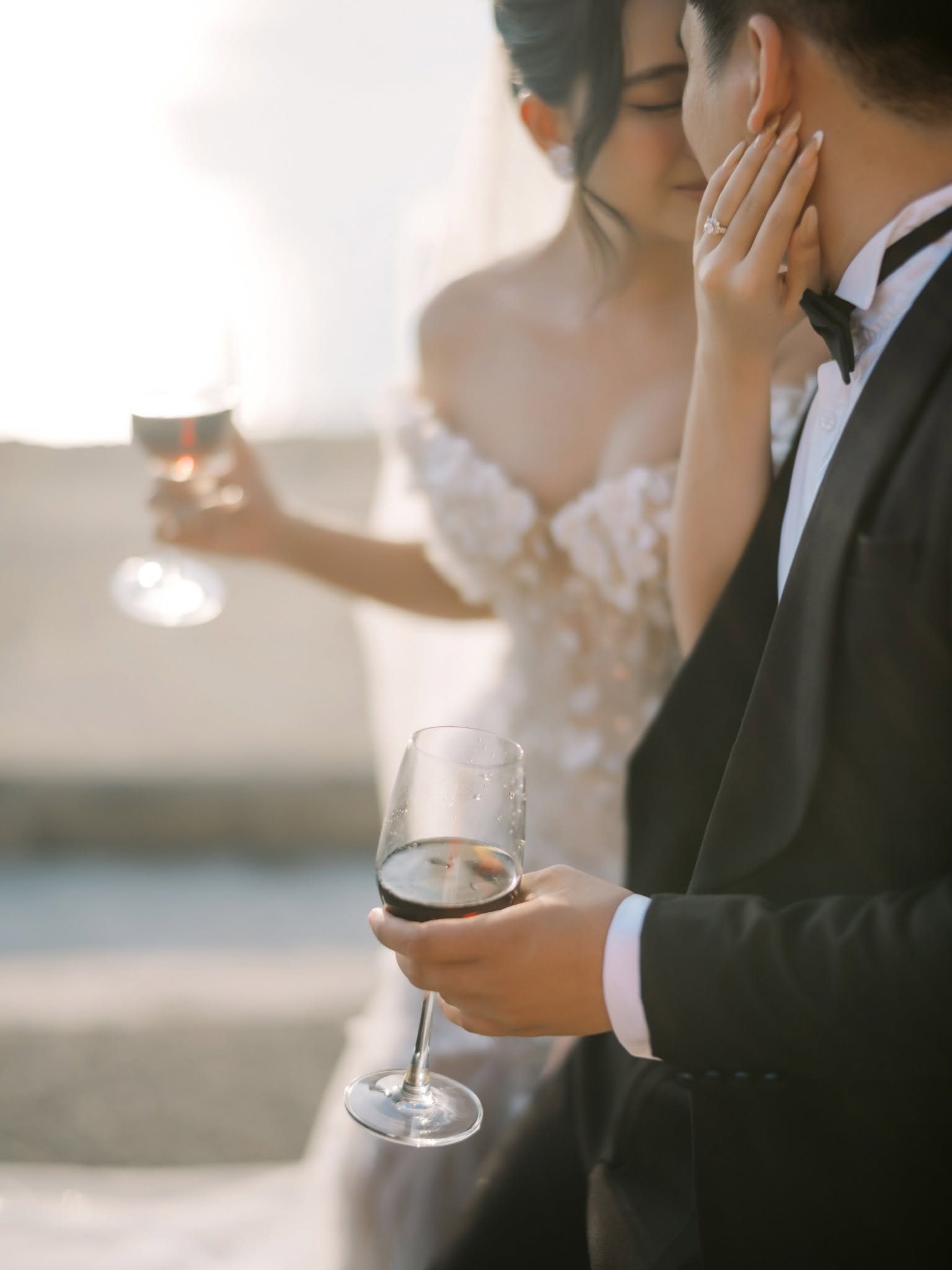 Foreheads close, glasses in hand, the sea glowing behind.