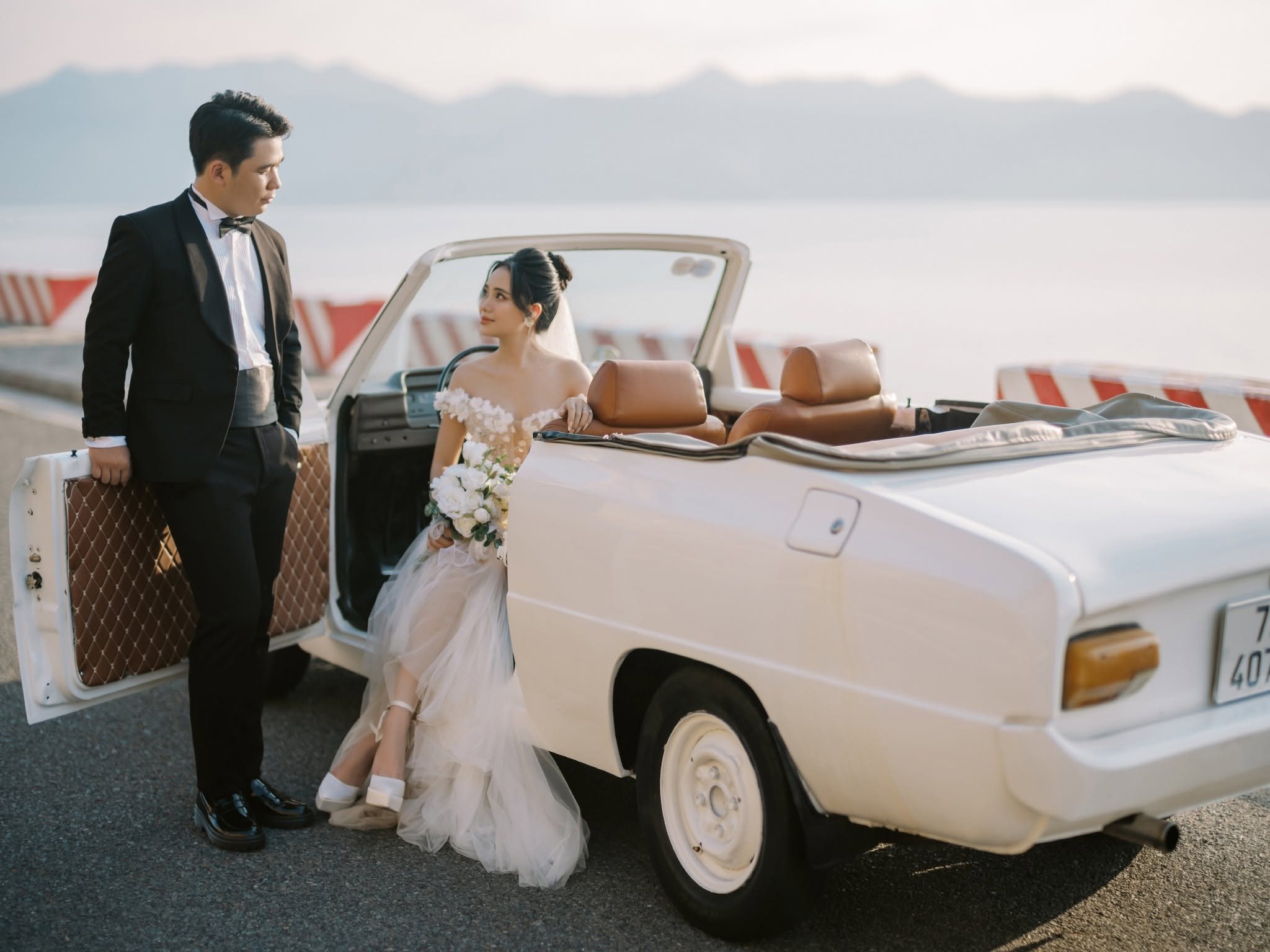 The convertible with its door open, sea and sky behind.