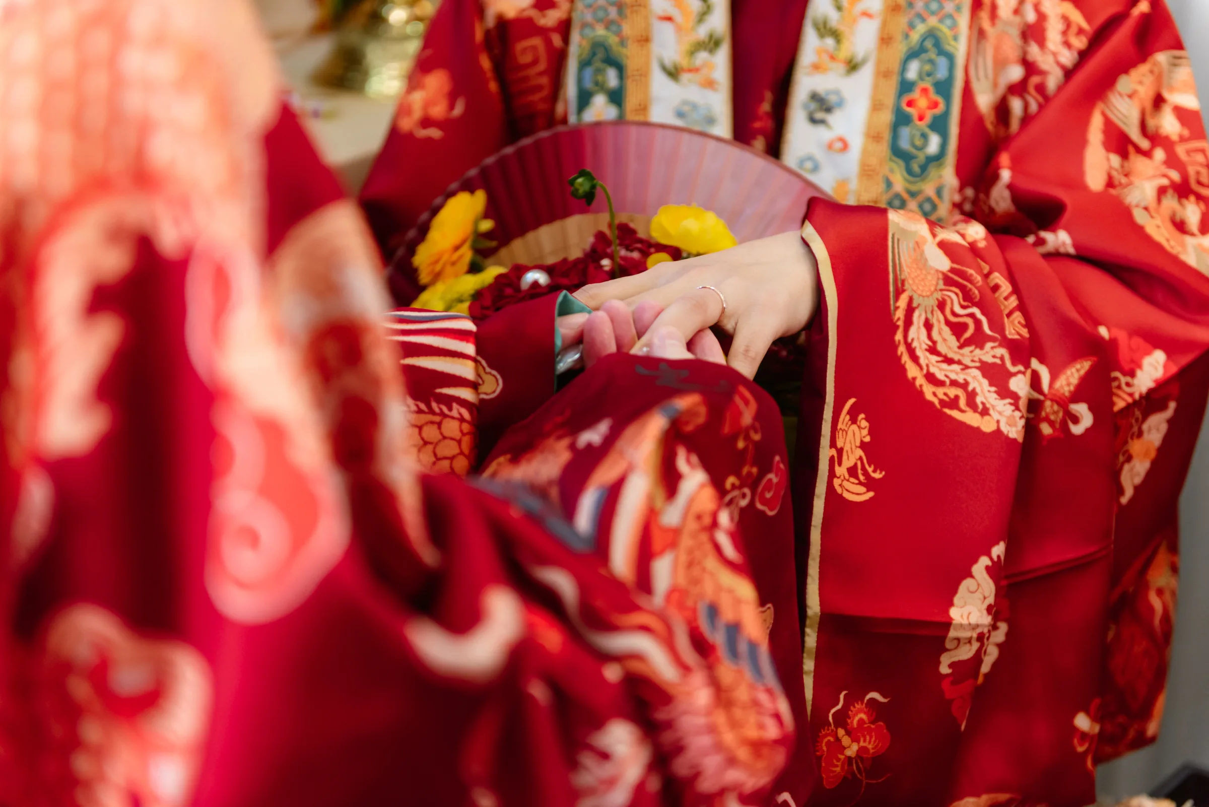 The rich detail of a bride's red brocade ao dai, hand-embroidered with dragon and phoenix motifs, at a Vietnamese wedding.