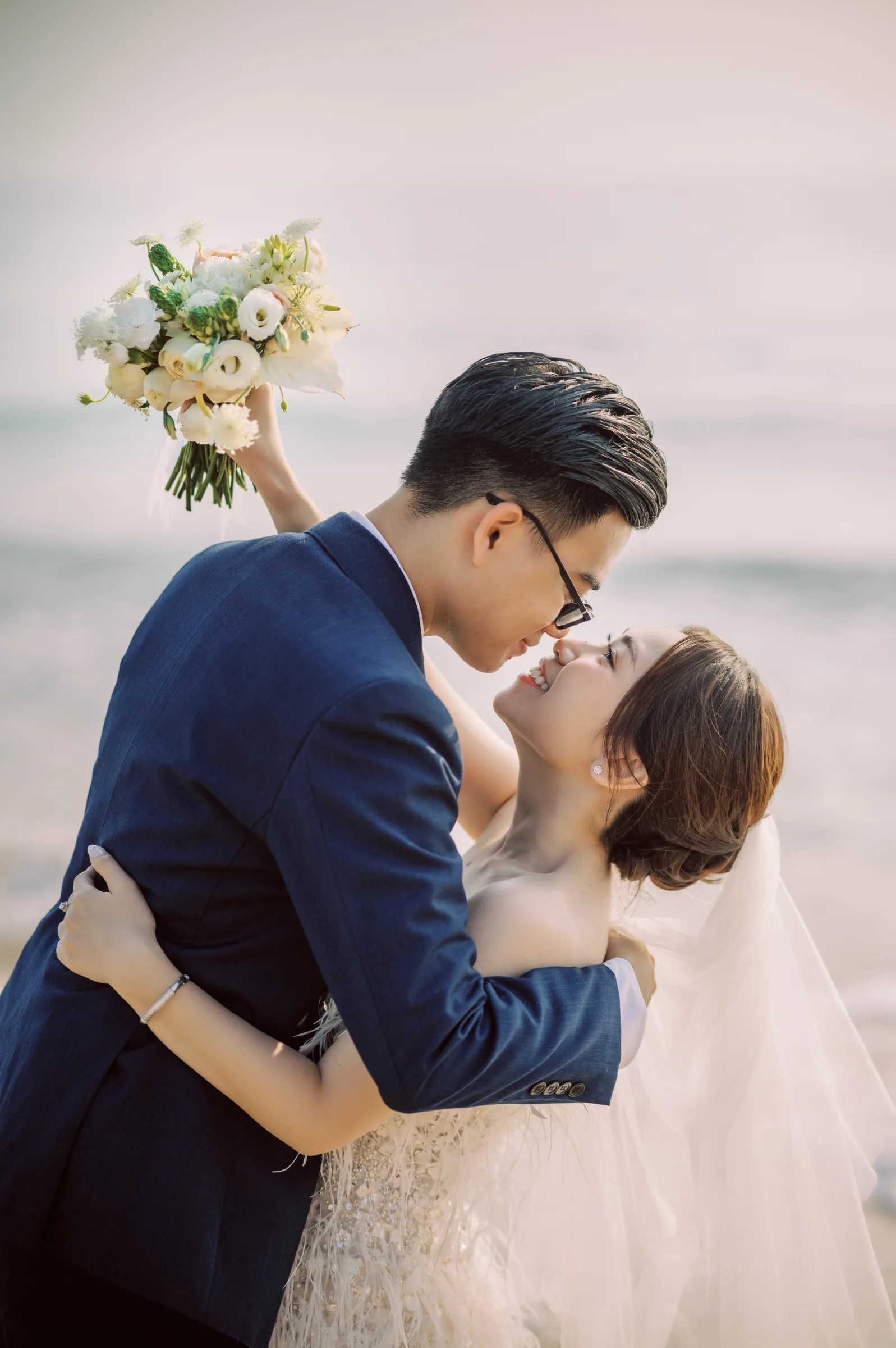 A couple embracing with a bouquet by the sea at a Phu Yen pre-wedding by TIMO Wedding