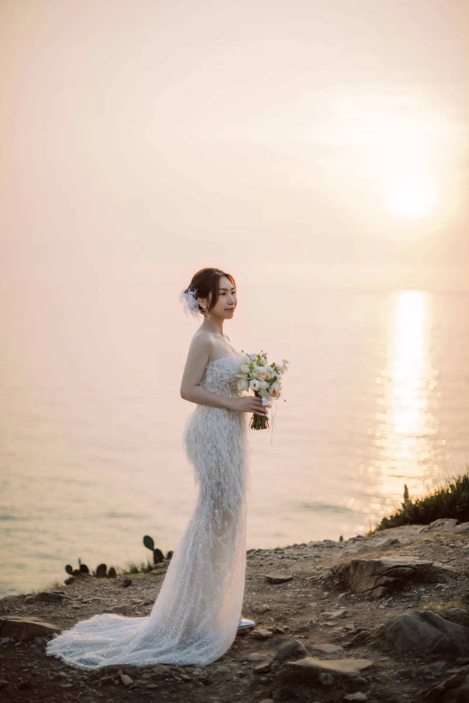 Bride with her bouquet on the cliffs as the sun sets over the sea, Phu Yen
