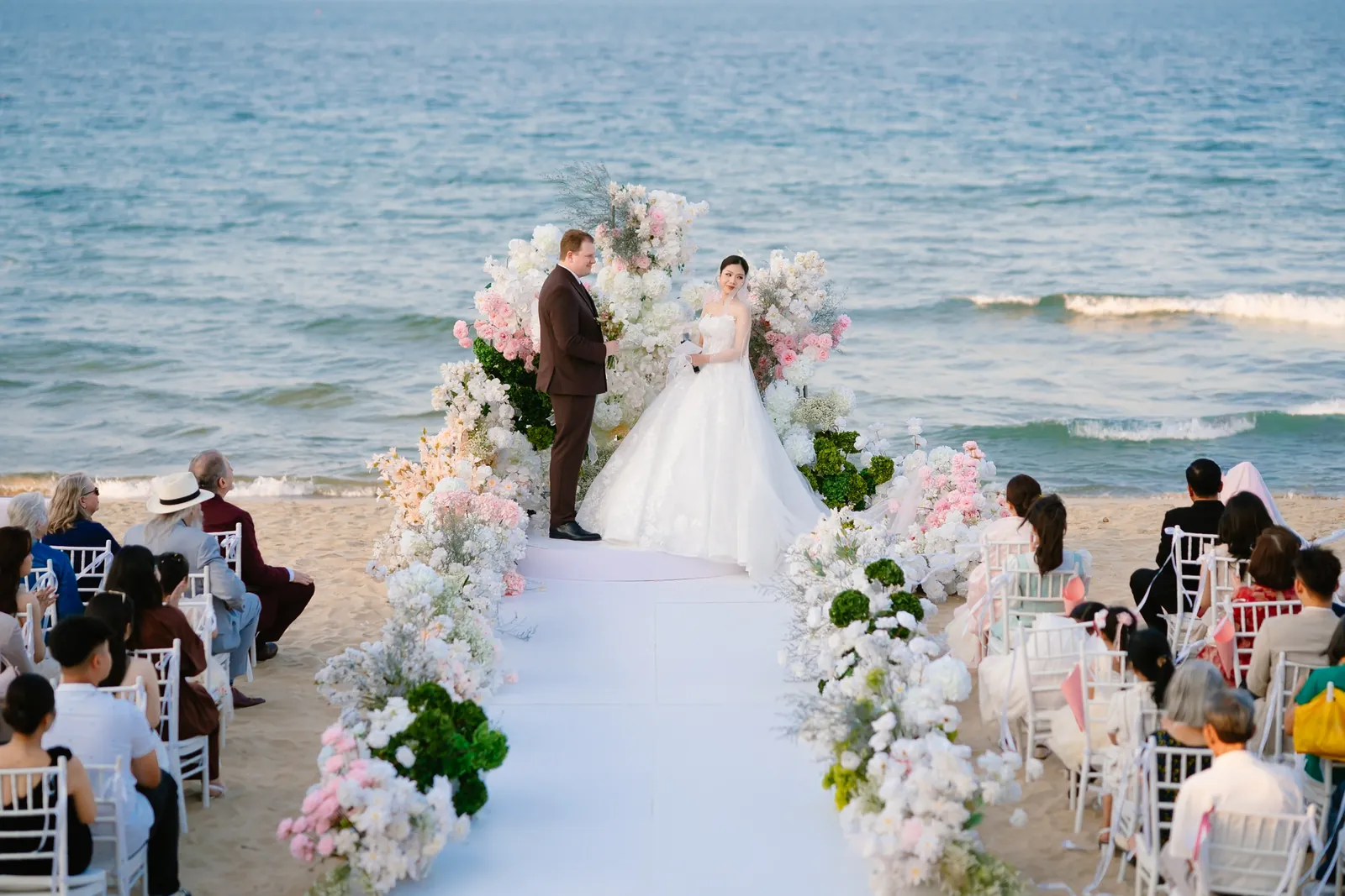 Vows at the floral arch, the sea just behind.